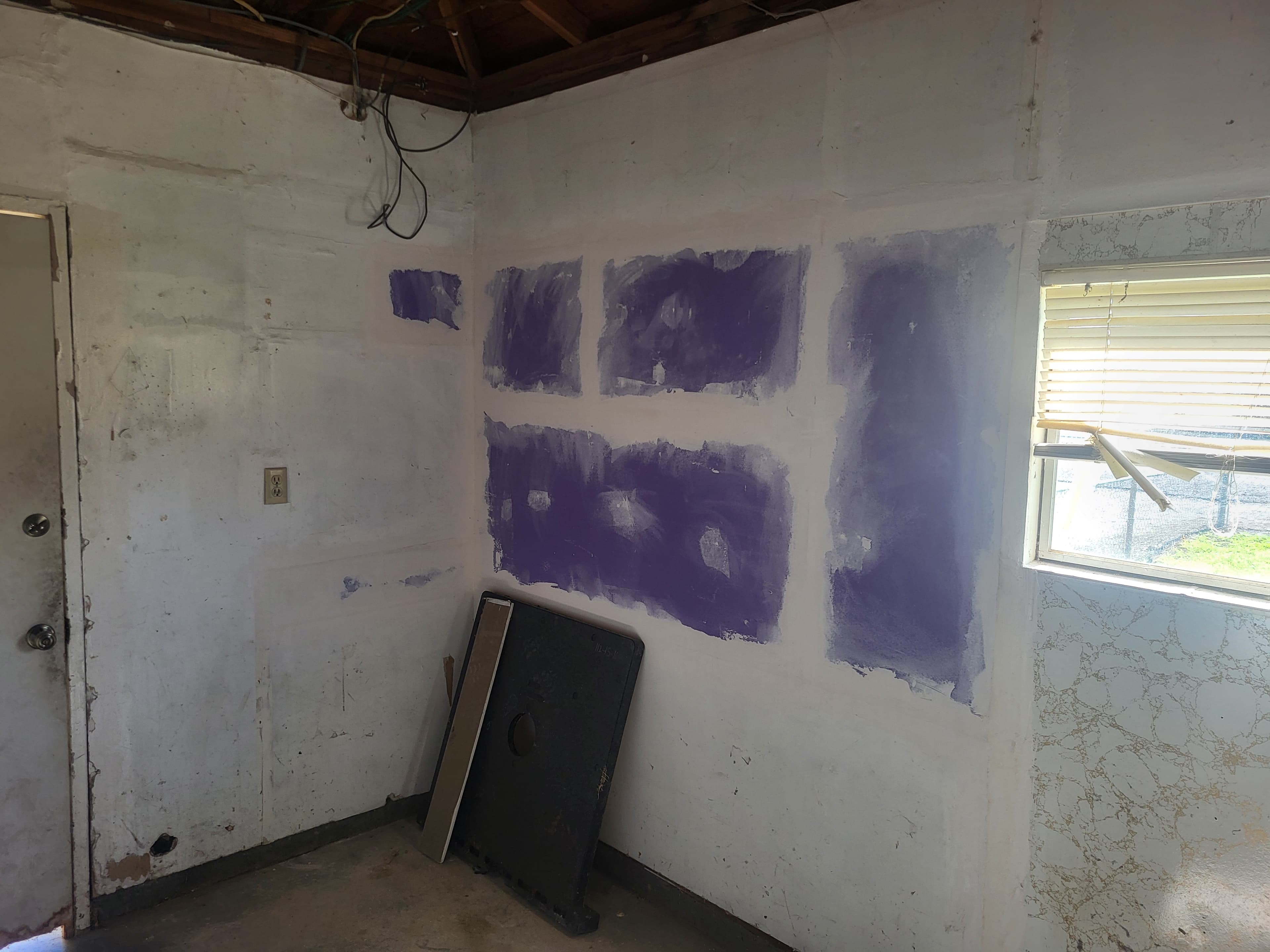 Interior room under renovation with purple paint patches on white walls and exposed ceiling wires.
